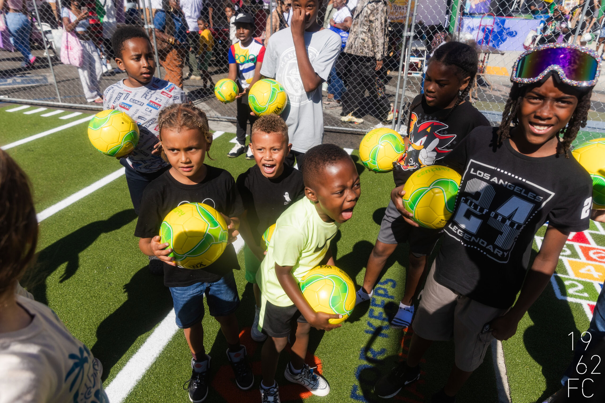 Kids holding soccer balls at outdoor sports event for children.