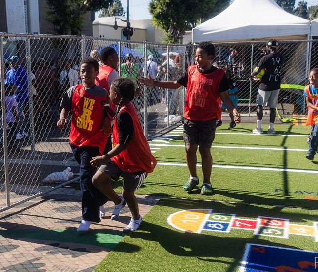 Kids playing soccer on a fenced sports field during daytime.