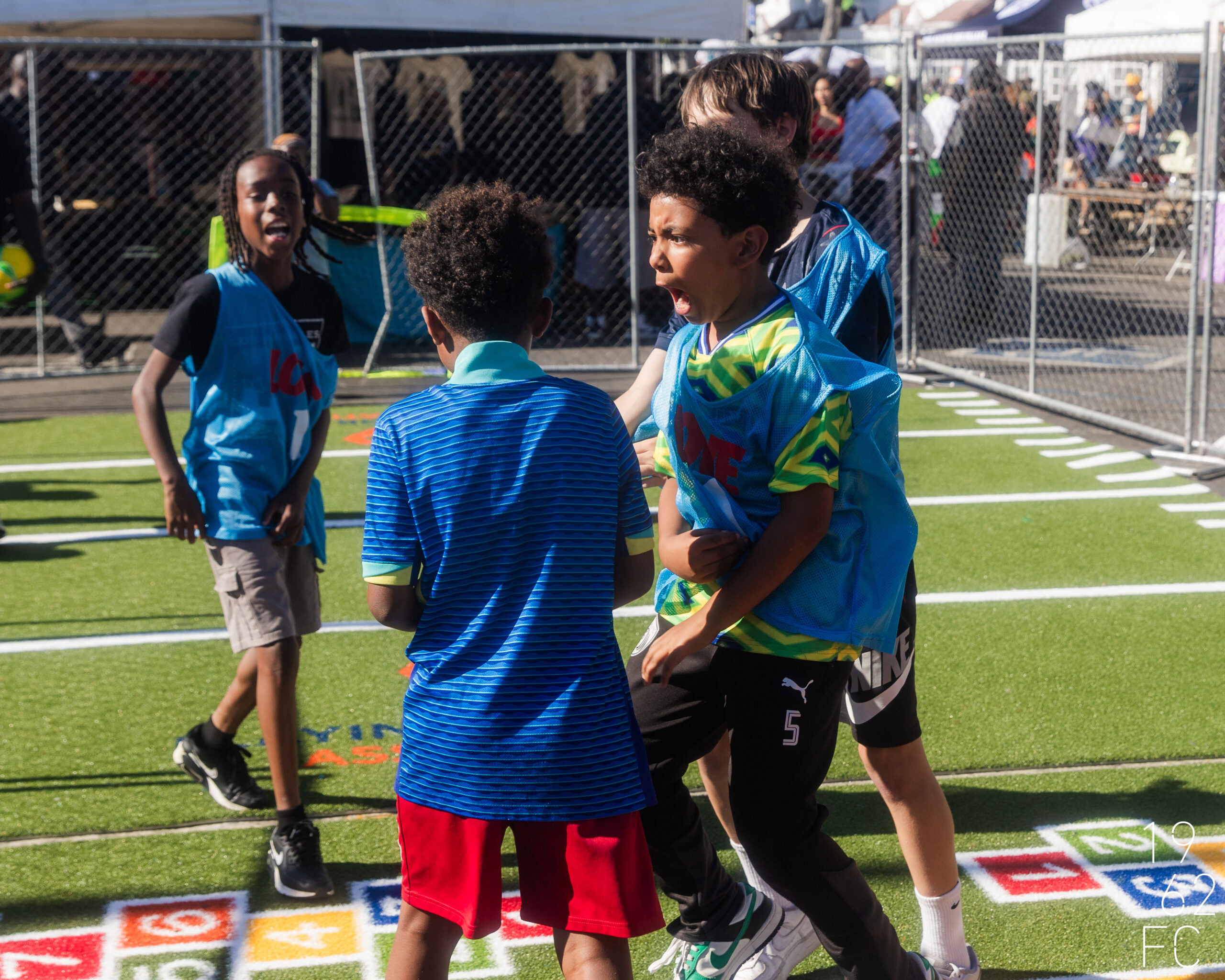 Kids playing soccer on artificial turf field during outdoor event.
