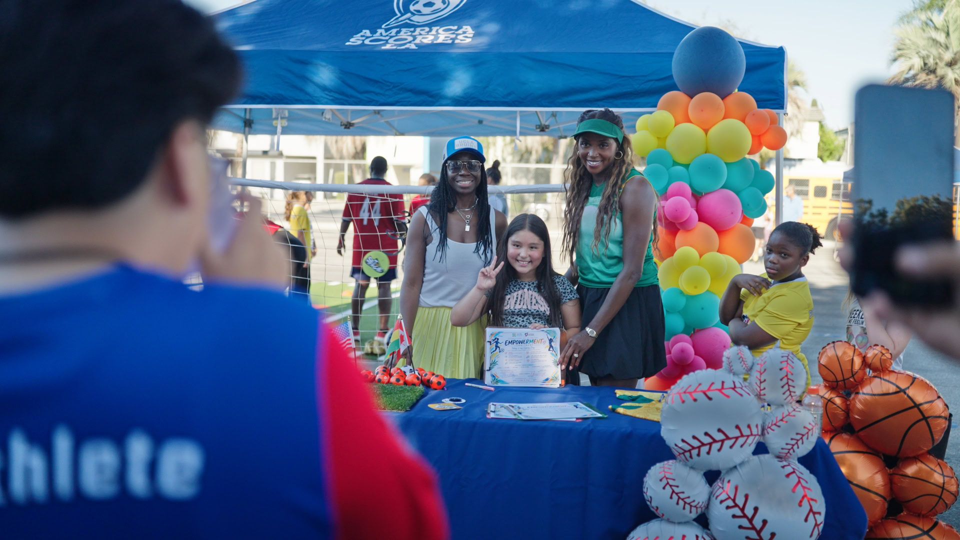 Community Event with Kids and Balloons Kids and adults at a community event with colorful balloons and sports-themed decorations.