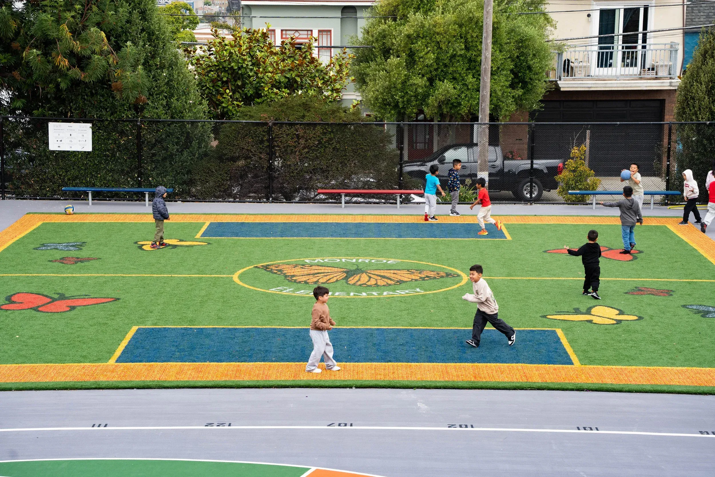 Children playing on a colorful outdoor synthetic field with a central emblem.