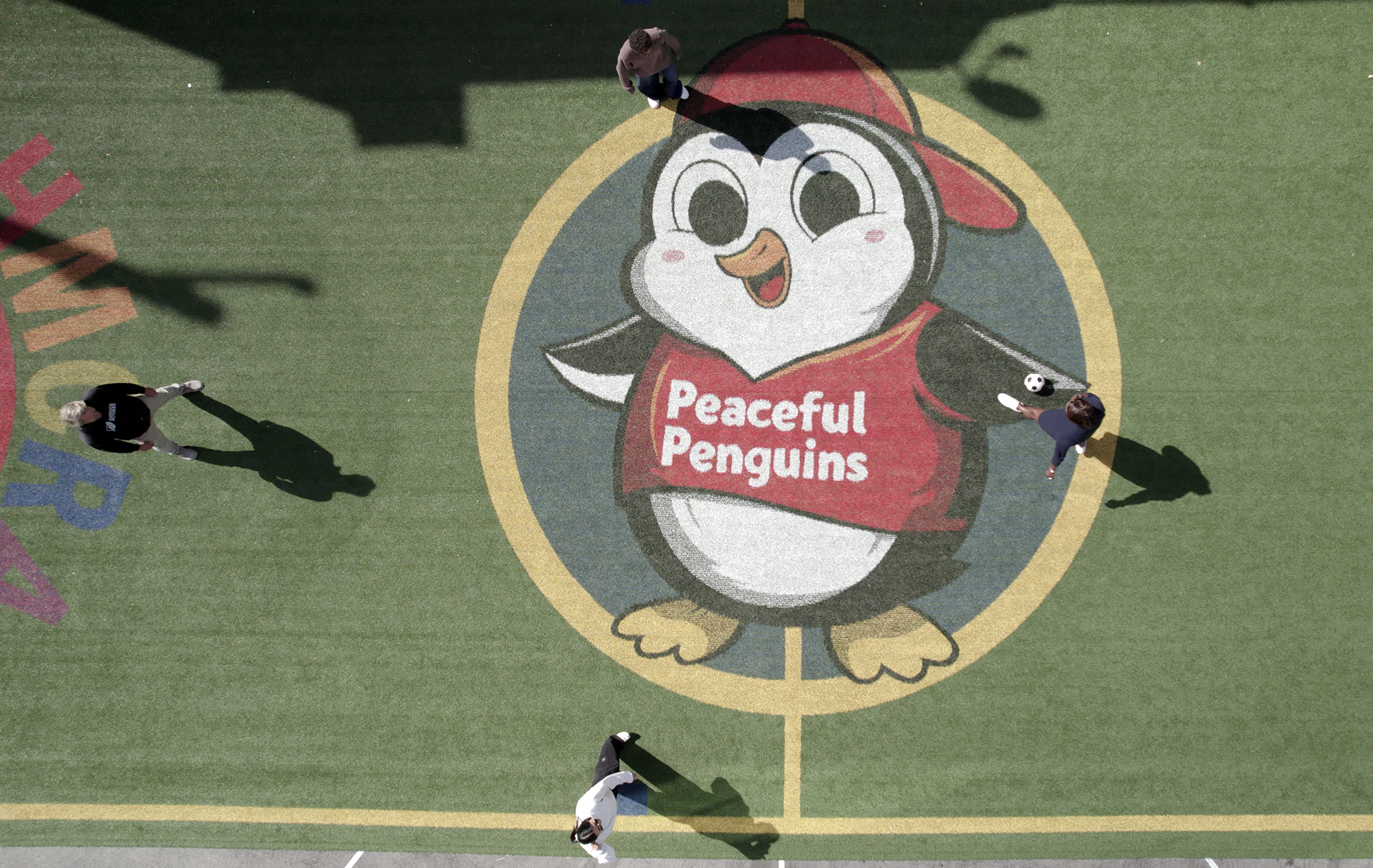 Aerial view of a penguin mascot logo on a sports field with players around.