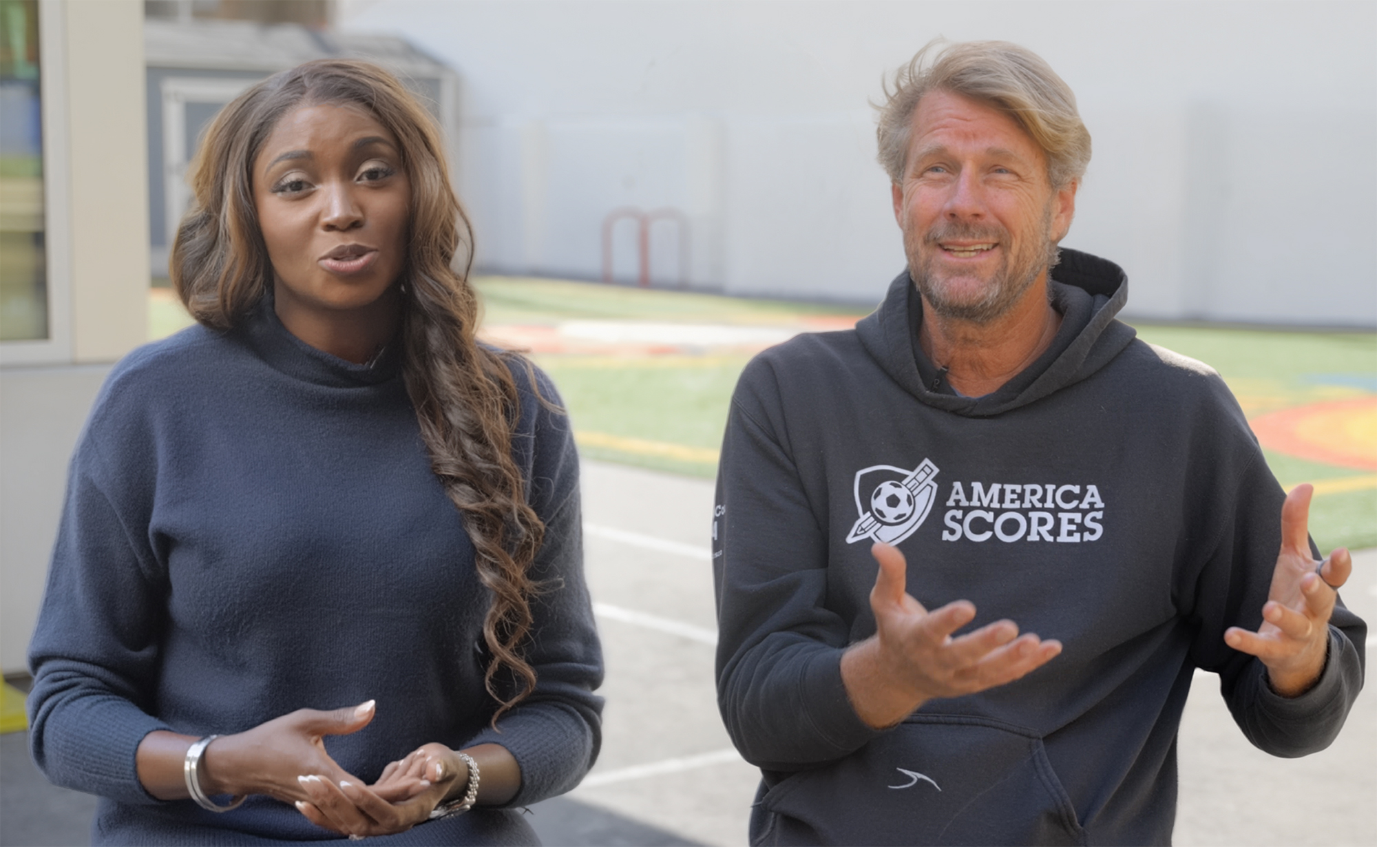 Two presenters discuss on set wearing casual branded apparel.