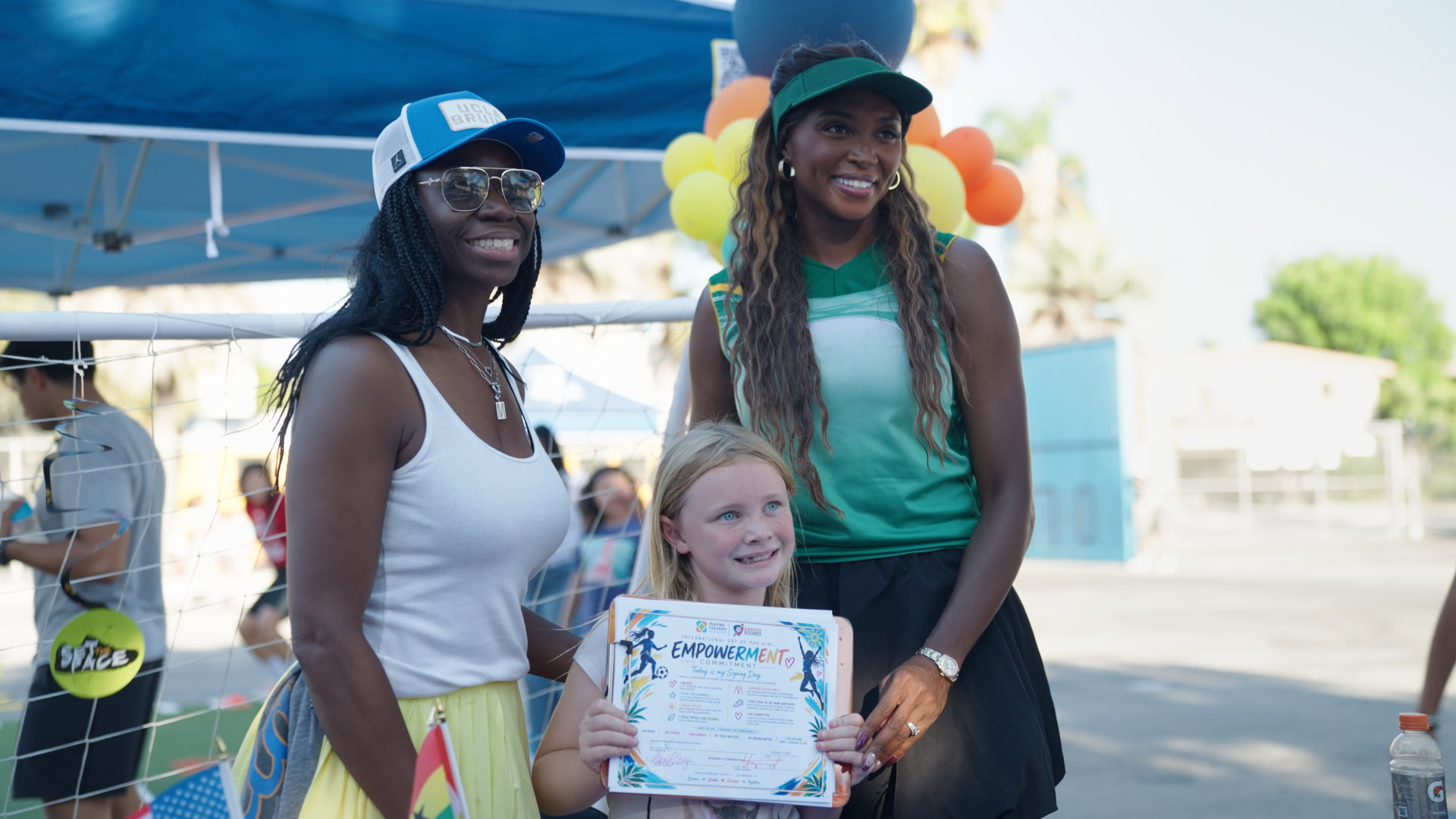 Two women and a girl holding a certificate at outdoor event.
