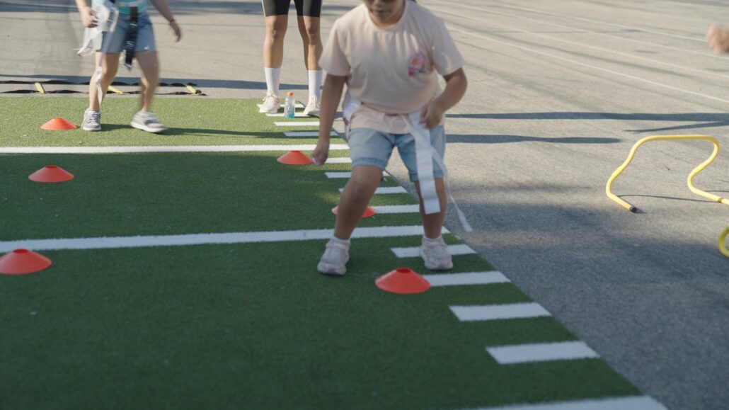 A girl runs a flag football agility drill on the temporary turf field.