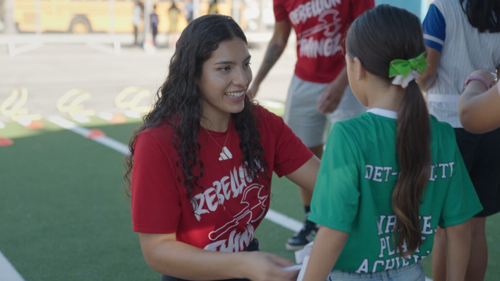 A San Diego Rebellion player talks with a young participant on the temporary turf field.